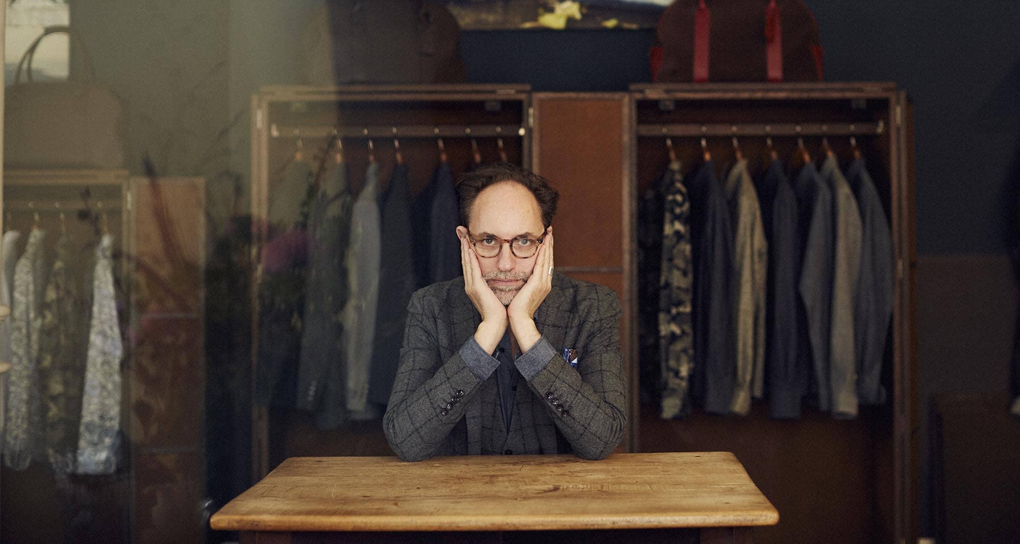 Herr Lewin sitzt an einem Tisch und schaut in die Kamera