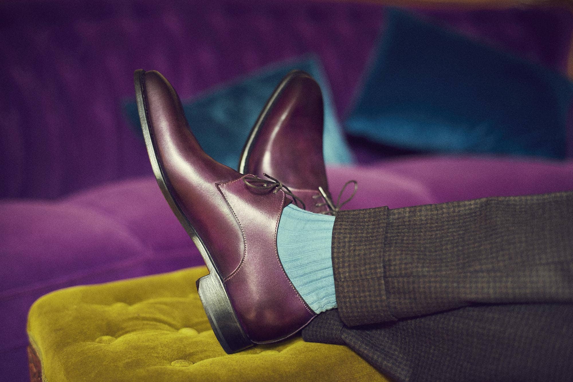 Füße liegen auf einem Hocker, mit roten Schuhen und grünen Socken